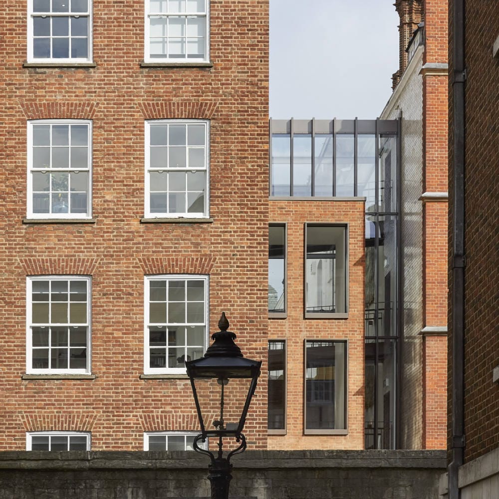 1000-Morey Smith_Blackstone Chambers_London_©Hufton+Crow_003 Brick buildings with rectangular windows and a modern glass extension between them. A vintage street lamp is in the foreground.