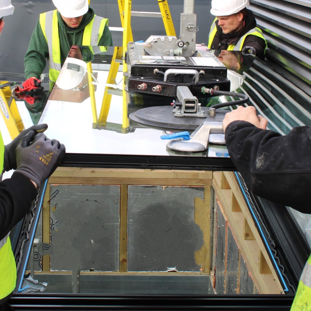 NGR Rooflight Installation with Crane and Installation Team Workers in high-visibility vests and hard hats install a large windowpane using suction lifters and other equipment at a construction site.