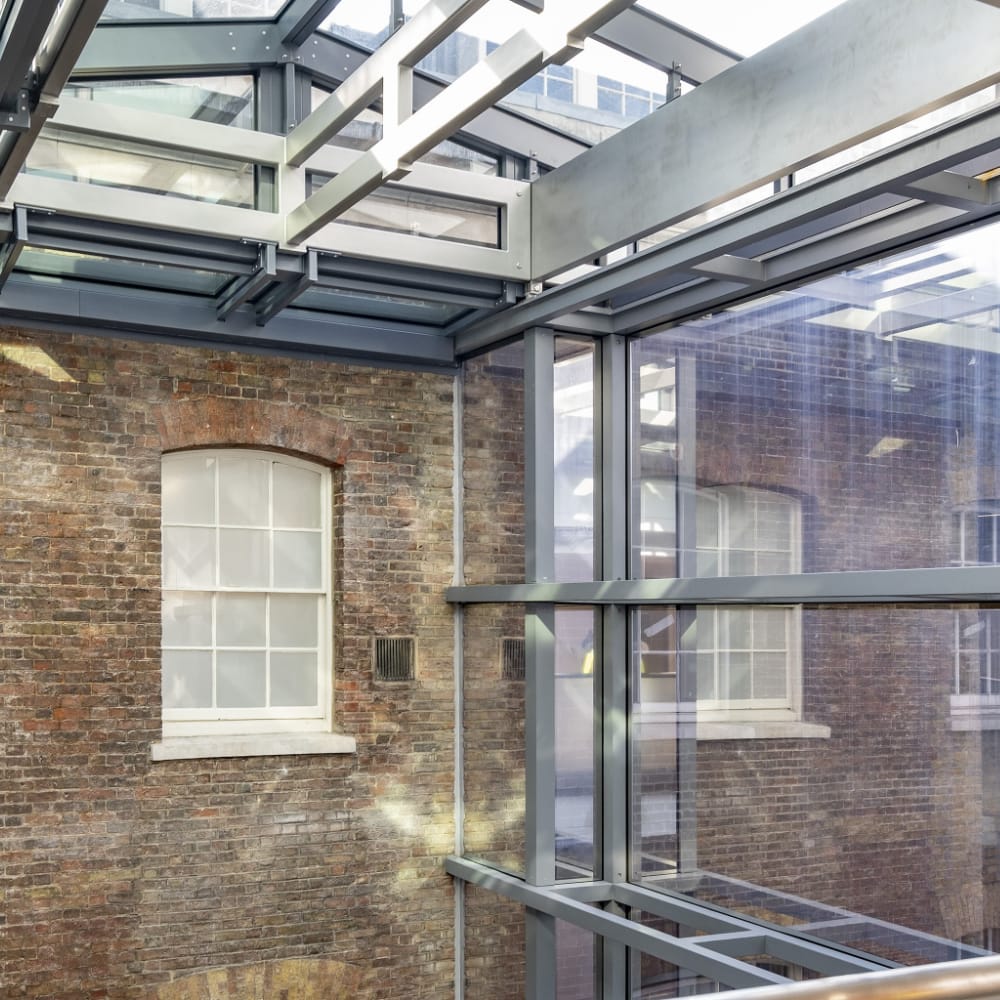 NGR Structal Glass Historic Commercial Renovation A glass and steel structure encloses a courtyard with brick walls and windows, blending modern and traditional architectural elements.