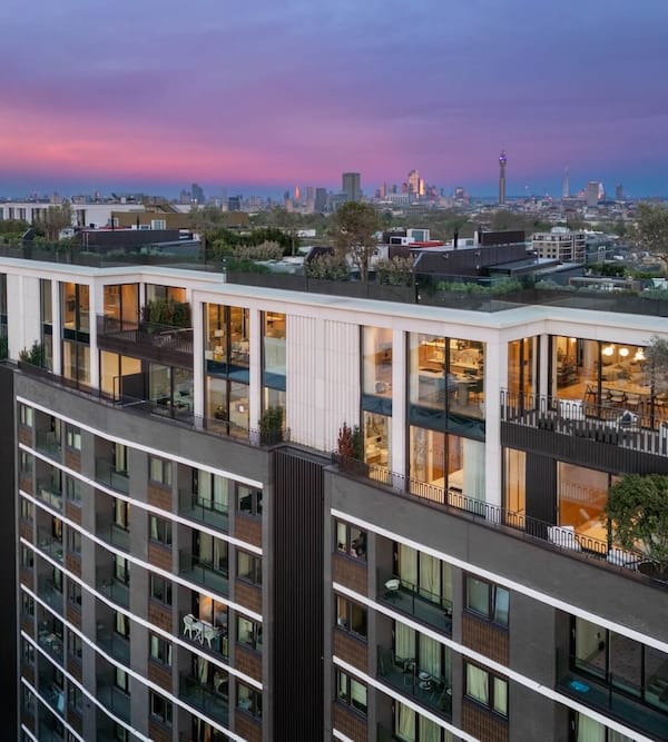 access A modern apartment building with large windows and rooftop greenery, set against a city skyline at dusk.